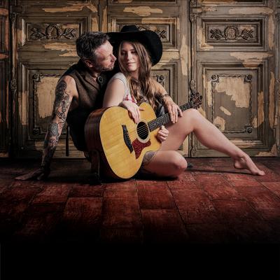 A picture of a man and woman sat on the floor with a guitar